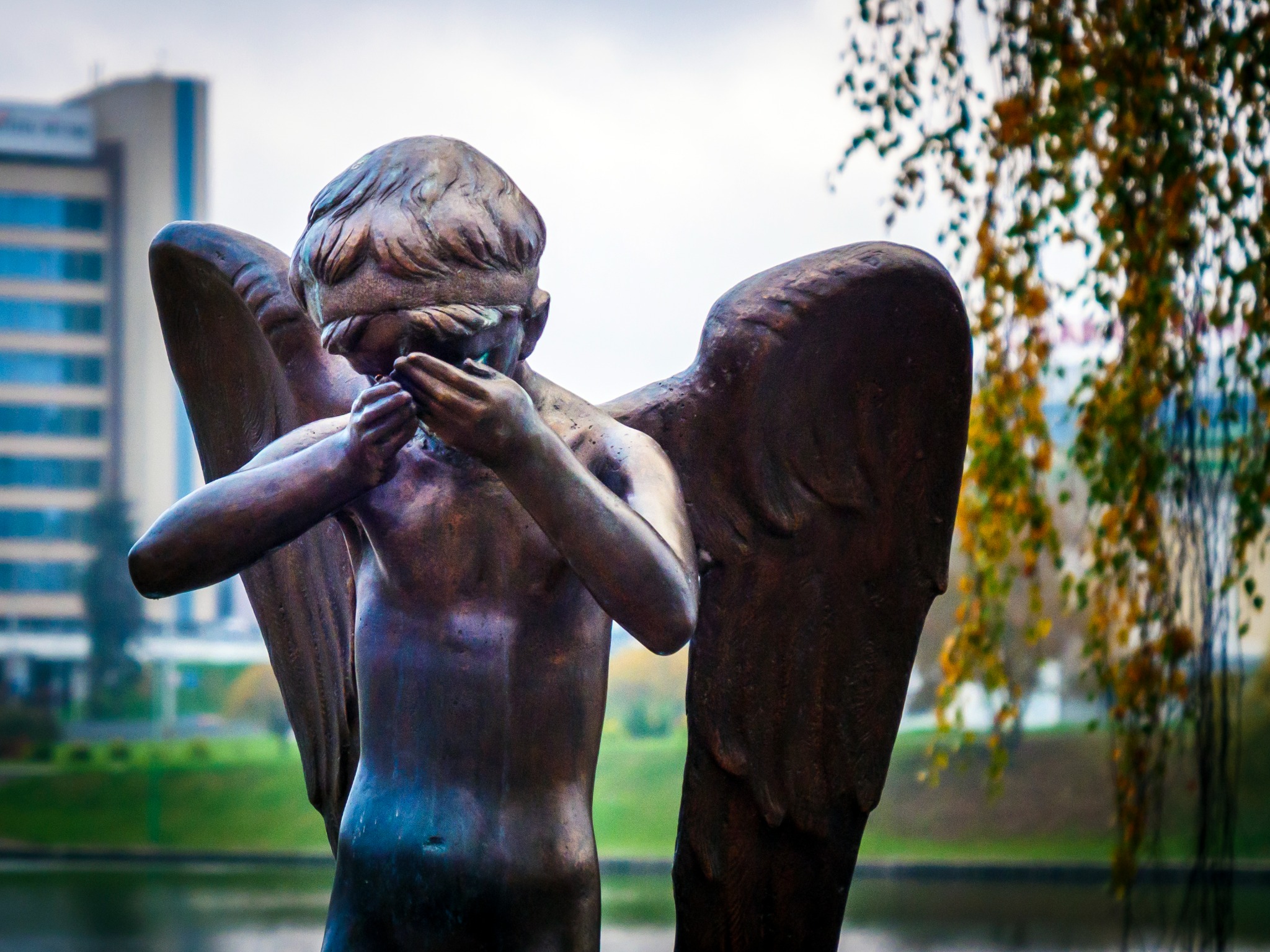 Skulptur av en bevingad gestalt med händerna framför ansiktet