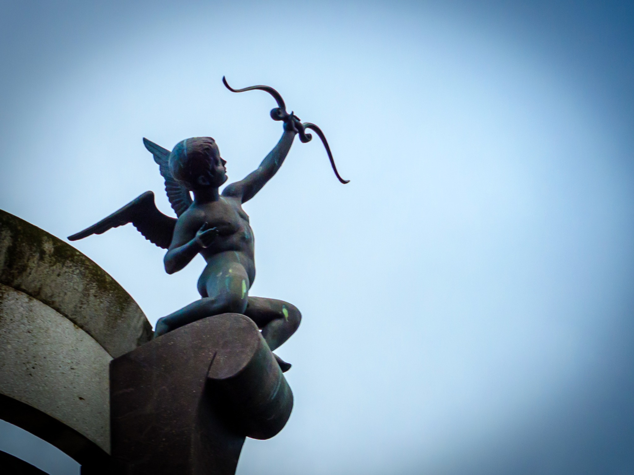 Bevingad skulptur som håller upp en båge mot himlen